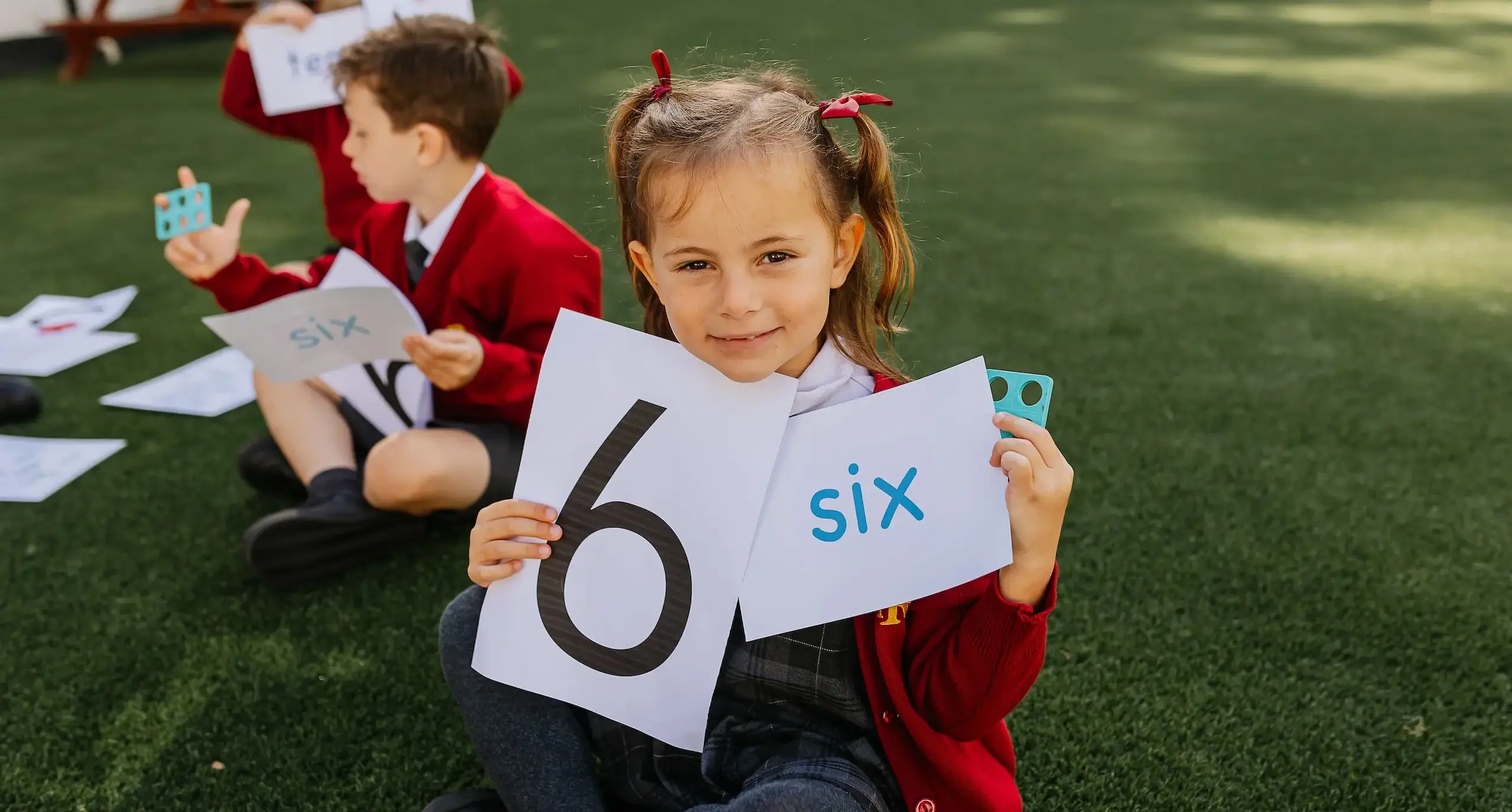 Student cross-legged on the floor, showing two flashboards that say 'six' and '6'