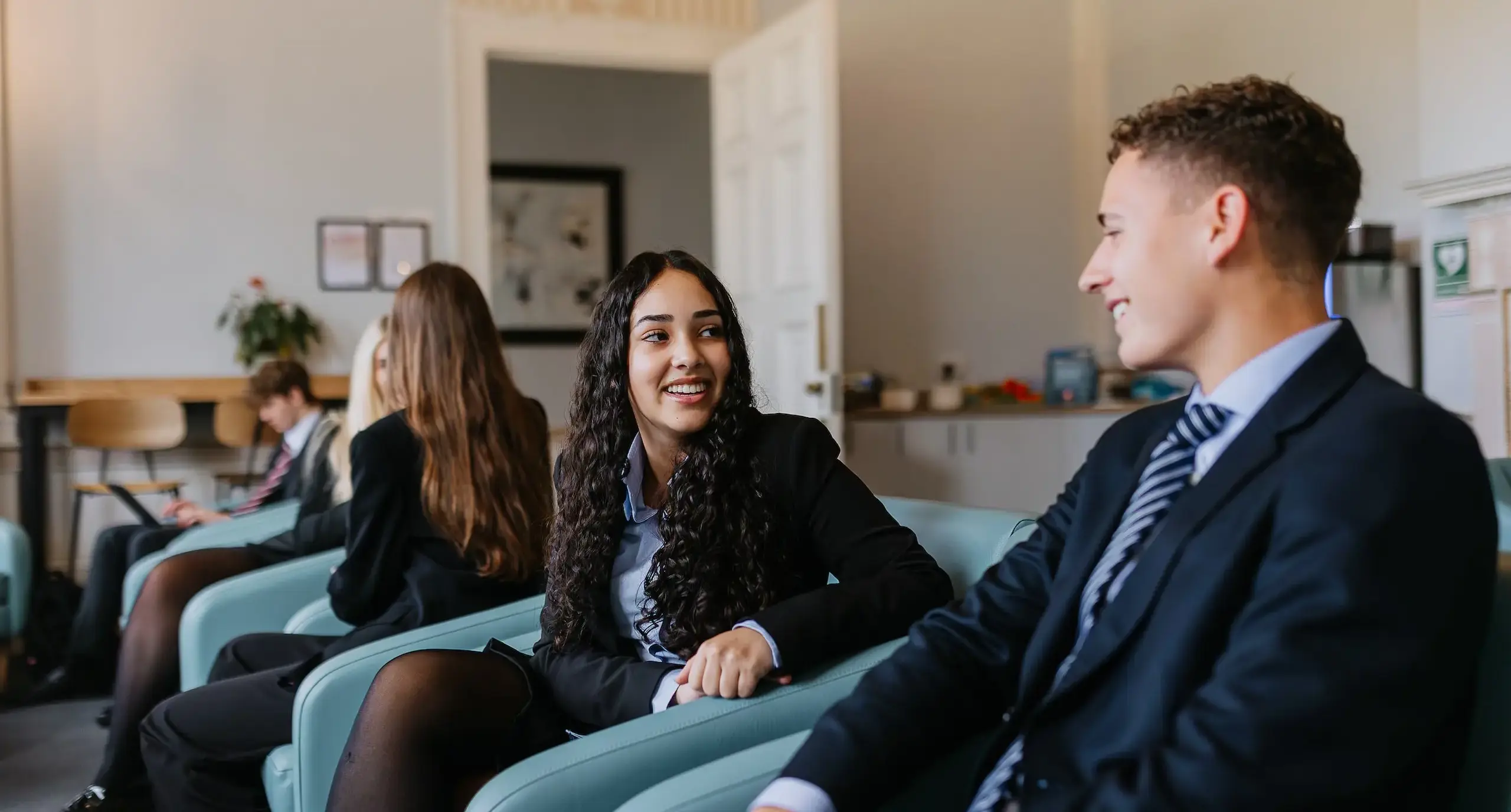 Radnor Sixth Formers conversing while sitting in light blue common room armchairs